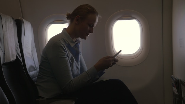 In vliegtuigmening van vrouw die met bankkaart betaalt die smartphone en dongle gebruikt voor het scannen van ban...