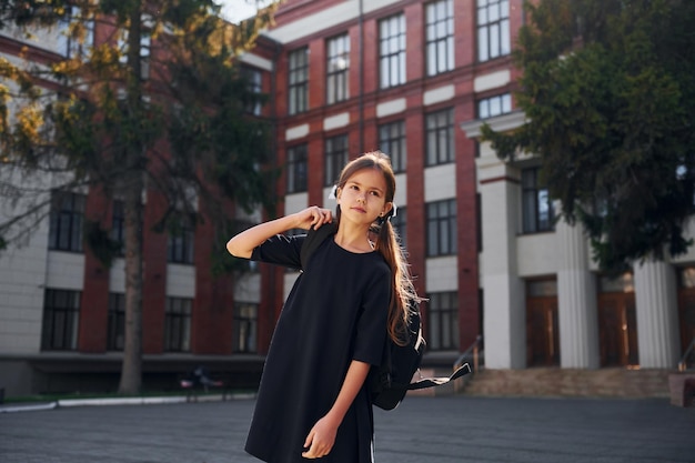 In zwart uniform staat Schoolmeisje buiten bij schoolgebouw
