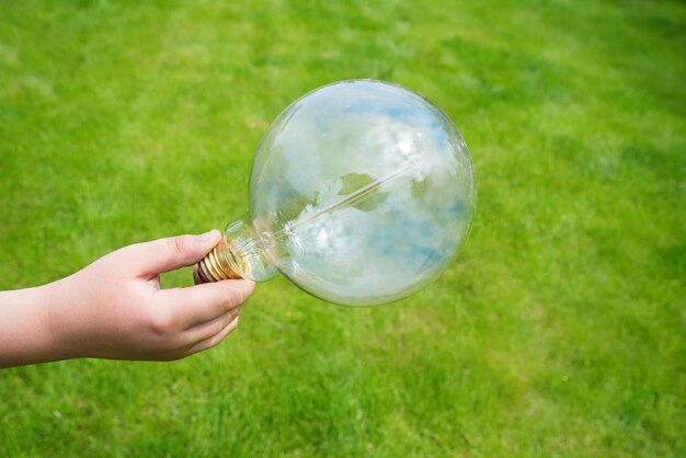 緑の草の背景に子供の手の中の白熱灯