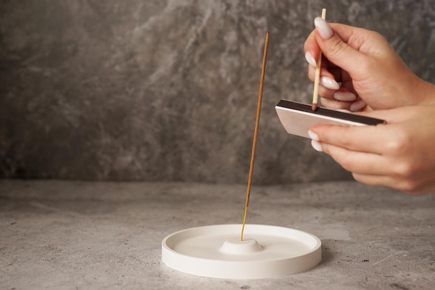 Incense stick in ceramic holder on marble table Hand with long matches