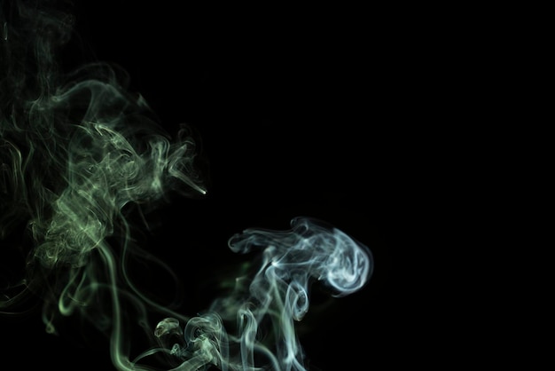 Incense stick with green smoke against black background