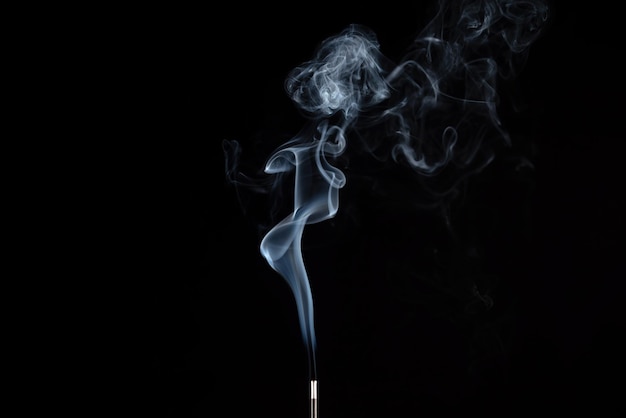 Incense stick with smoke against black background