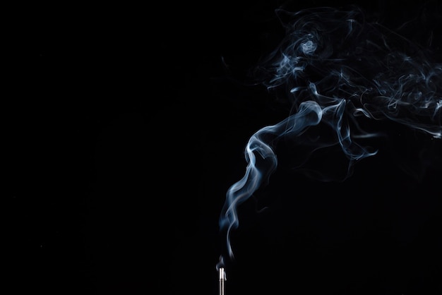 Incense stick with smoke against black background