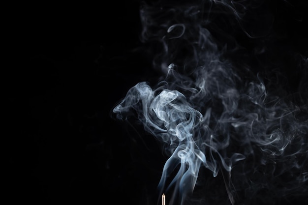 Incense stick with smoke against black background