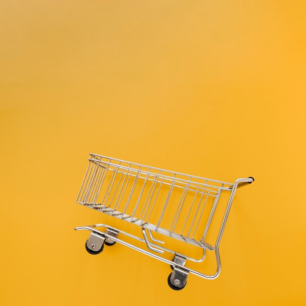 Photo inclined shopping cart in yellow background