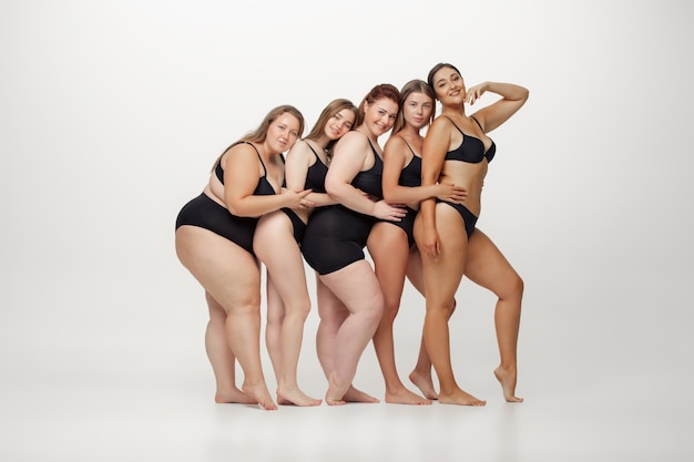 Inclusion. Portrait of beautiful young women with different shapes posing on white background. Happy female models. Concept of body positive, beauty, fashion, style, feminism. Diversity.