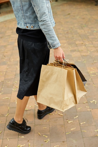 Foto donna in incognito che tiene in mano diversi sacchetti di carta che cammina all'aperto nel parco