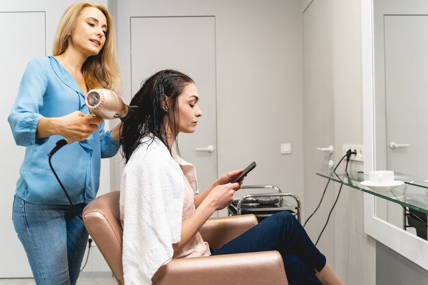 Income message. Professional hairdresser standing behind her client while drying soft hair, talking about beauty industry