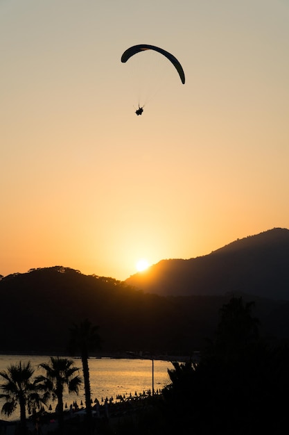 Incredible mountain scenery with the beach reflecting the evening sun and the silhouette of a paraglider flying in the sky