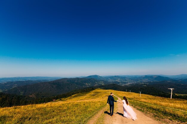 An incredible view of the mountains with forests and the horizon and newlyweds who descend from the top of the mountain and hold hands