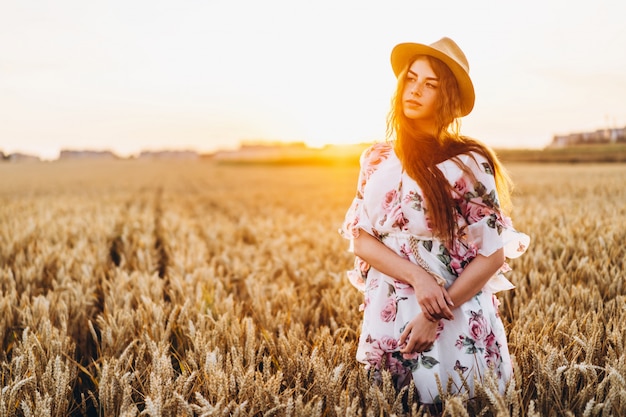 長い巻き毛とそばかすのある顔を持つ信じられないほどの若い女性。夕暮れ時の麦畑でポーズをとってドレスを着た女性。ポートレートを閉じる