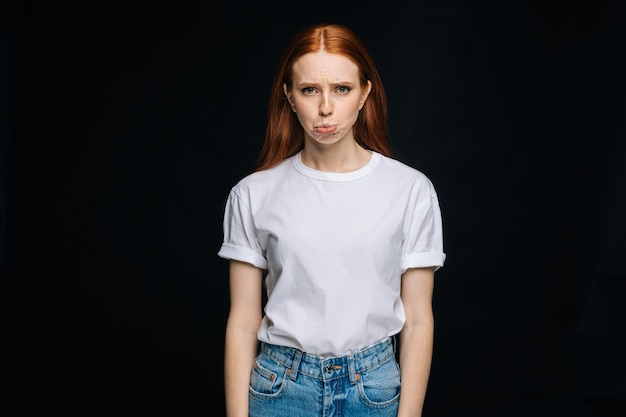 Indecisive young woman wearing tshirt and denim biting lips apologizing on isolated back background