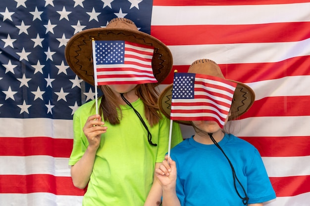 독립 기념일. 애국적인 휴일입니다. 행복한 아이들, 미국 국기를 든 귀여운 두 소녀. 카우보이. 미국은 7월 4일을 축하합니다. 깃발로 얼굴을 가린 소녀들