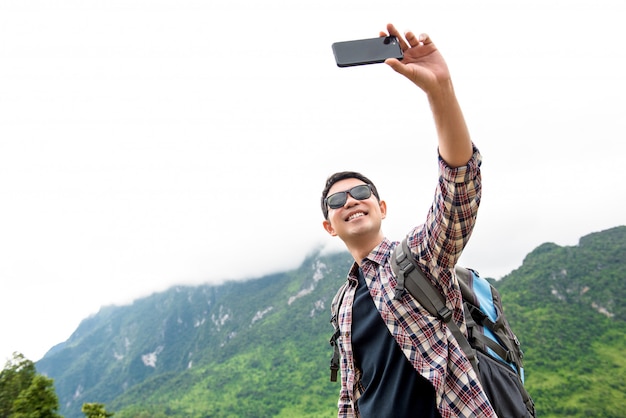 自然の緑の山の風景とselfieを取っている独立したアジアの観光客男性