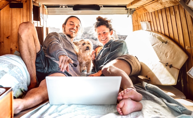 Independent couple with cute dog using laptop on retro mini van transport