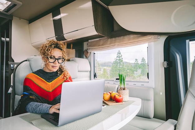 Independent woman sitting inside a camper van in smart remote working job activity using laptop Concept digital nomad freedom lifestyle with female people writing on computer Outdoors view outside