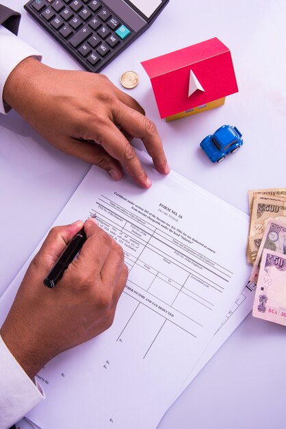 Photo india and accounting concept showing accountant working on income tax forms with currency notes, calculator and house and car 3d models