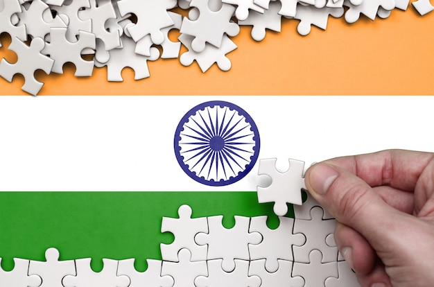 La bandiera dell'india è raffigurata su un tavolo su cui la mano umana piega un puzzle di colore bianco