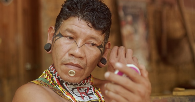 indiaan van de pataxo-stam met behulp van een spiegel en schminken