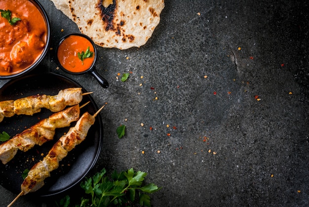 Indiaans eten. traditionele gerecht pittige kip tikka masala, boter kip curry, met indiase naan boter brood, specerijen, kruiden. gediend in kom. saus, op spiesjes. stenen donkere tafel. copyspace bovenaanzicht