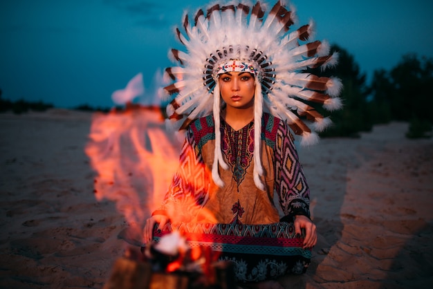 Indiaanse meisje tegen vreugdevuur in de nacht, vrouwelijke sjamaan, cherokee, navajo. hoofdtooi gemaakt van veren van wilde vogels. traditioneel ritueel