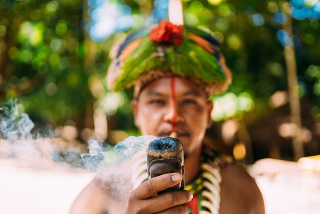 Indiaanse opperhoofd van de PataxÃ³ stam rookpijp. Braziliaanse Indiaan met veren hoofdtooi en ketting camera kijken