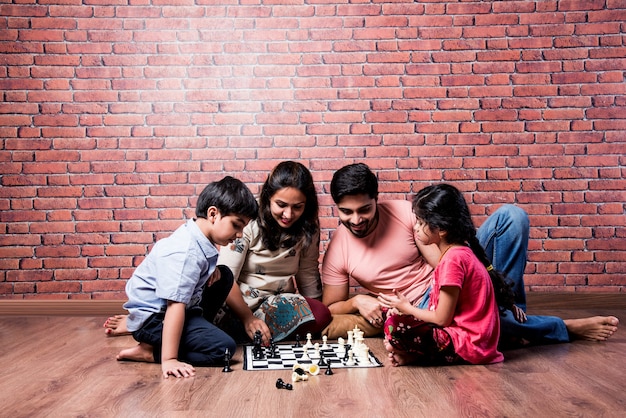 Indiaas jong gezin van vier die bordspellen zoals schaken, ludo of snack en ladder spelen thuis in quarantaine