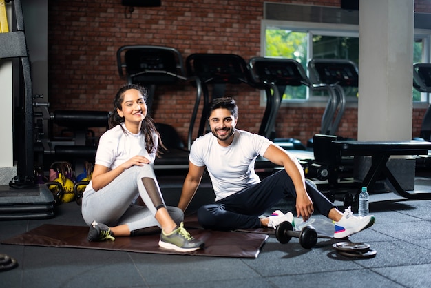 Indiaas jong stel in de sportschool die rust of een pauze neemt van het sporten, water drinkt, positieve uitdrukkingen toont