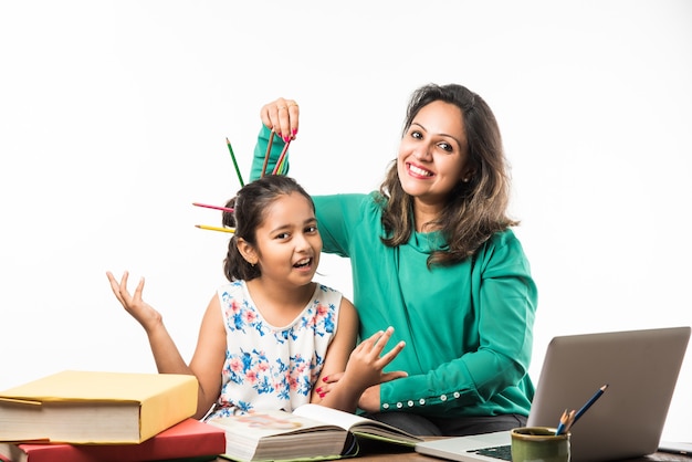 Indiaas meisje studeert met moeder of leraar aan studeertafel met laptopcomputer, boeken en heeft plezier bij het leren