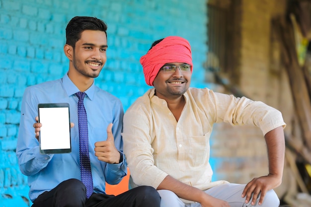 Agronomo indiano che mostra lo schermo del tablet con l'agricoltore a casa