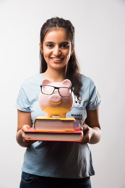 Photo indian asian attractive female student with holding piggy bank over green chalkboard background with doodles, selective focus