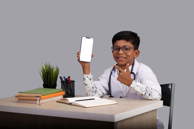 손가락으로 가리키는 모바일 앰프를 보여주는 청진기를 들고 의사 앞치마를 입은 인도 아시아 소년