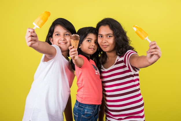 Indian or Asian cute little kids eating Ice cream or mango bar or candy. Isolated over colourful background