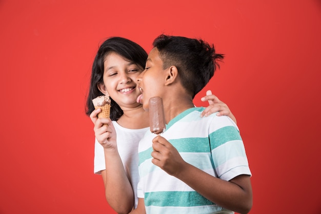 アイスクリームやマンゴーバーやキャンディーを食べるインドやアジアのかわいい子供たち。カラフルな背景の上に分離