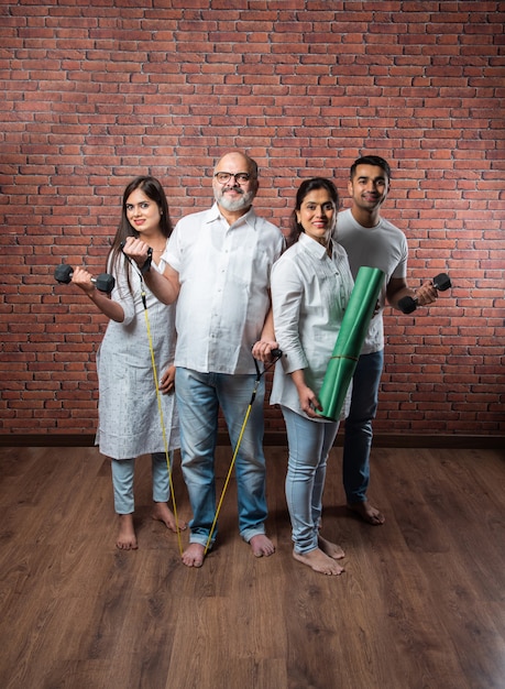 Famiglia asiatica indiana che si esercita a casa. senior genitori con bambini piccoli che fanno yoga, sollevamento pesi, utilizzo di theraband nell'interno del soggiorno. concetto di allenamento indoor