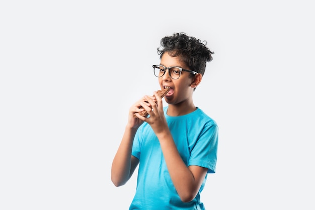 Indian asian happy boy eating chocolate slab, standing isolated against white wall