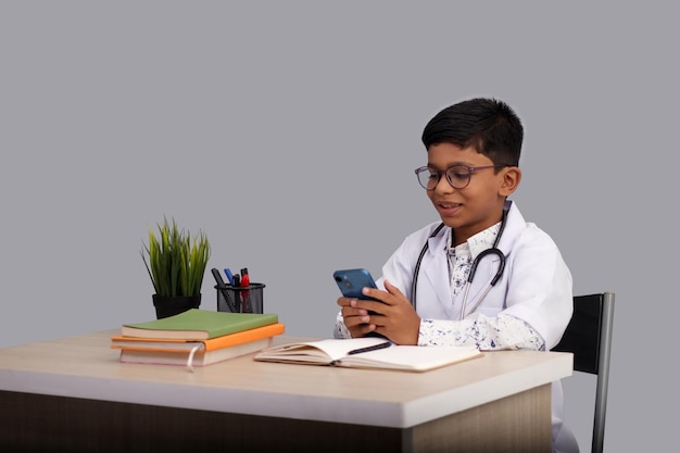 Photo indian asian kid boy aged 7 to 8 wearing a doctor apron with stethoscope watching in mobile