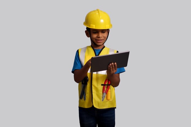 Photo indian asian kid boy aged 7 to 8 wearing a yellow helmet and safety jacket holding tablet in hand