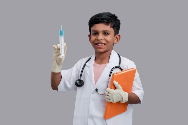写真 ドクターエプロンを着て聴診器を持ち、ブックアンプの注射をしている7〜8歳のインドのアジア人の少年