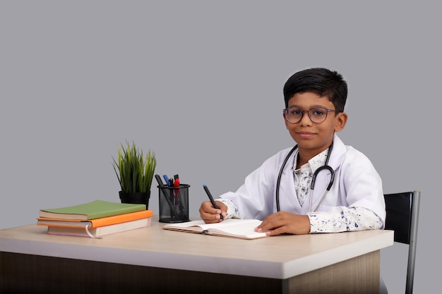 写真 聴診器を持ったドクターエプロンを着て処方箋を書く7歳から8歳のインドのアジア系少年