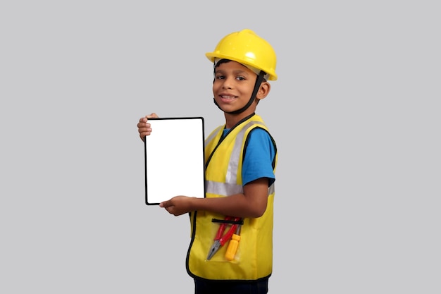 写真 黄色いヘルメットとセーフティジャケットを着て ⁇ 手にタブレットを握っている7〜8歳のアジア系少年 ⁇