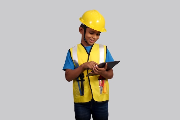 사진 7~8살의 아시아 소년은 노란색 헬 ⁇ 과 안전 재 ⁇ 을 입고 손에 태블릿을 들고 있다.