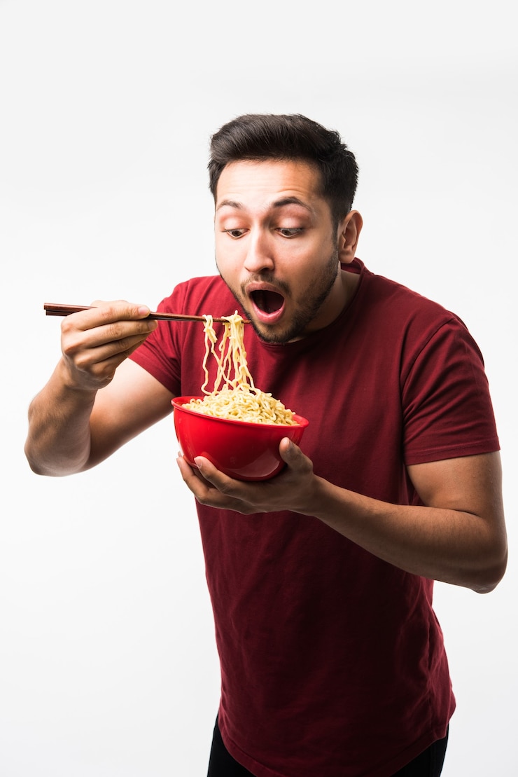 Photo 箸で赤いボウルに熱い麺やラーメンを食べるインドのアジア人男性