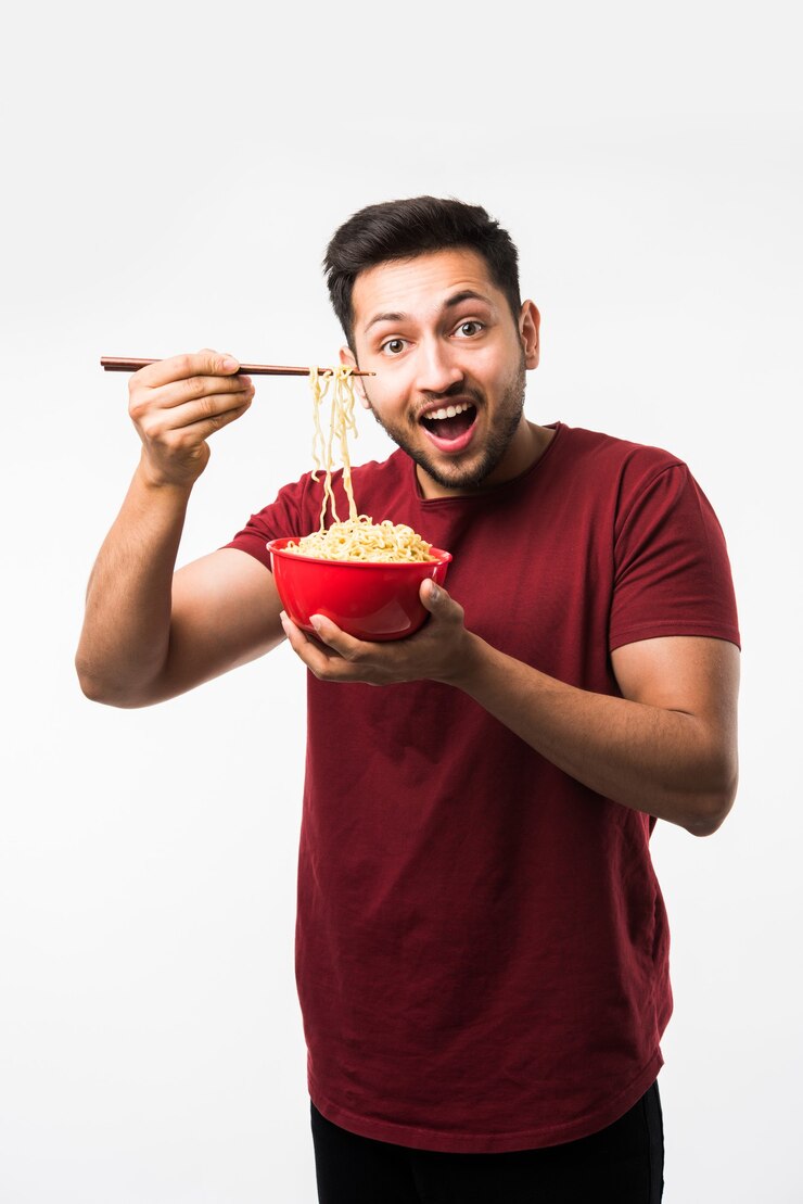 Photo 箸で赤いボウルに熱い麺やラーメンを食べるインドのアジア人男性