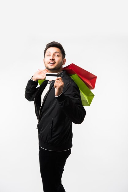 Indian asian man showing his shopping bags and credit or debit card while standing over white background