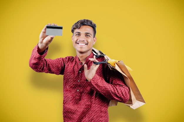 Indian asian man showing his shopping bags and credit or debit card while wearing traditional cloths standing over yellow background