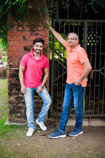 Indian asian senior father son, posing for photograph while wearing jeans and T-shirt, against red brick wall