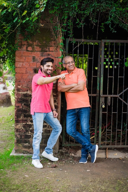 Indian asian senior father son, posing for photograph while wearing jeans and T-shirt, against red brick wall