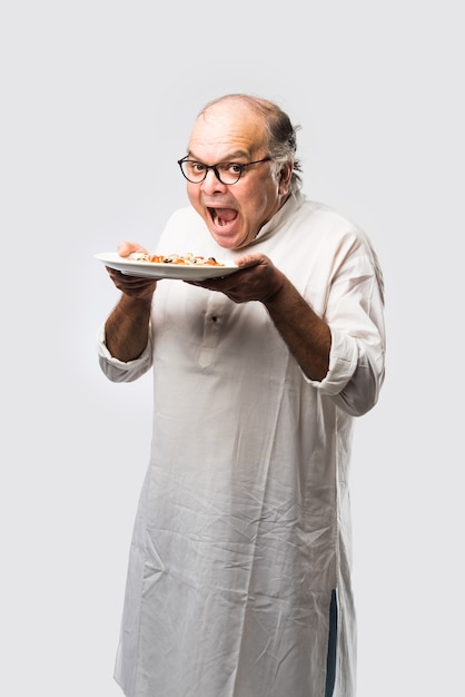 Indian asian senior or old man eating pizza while standing isolated against white wall