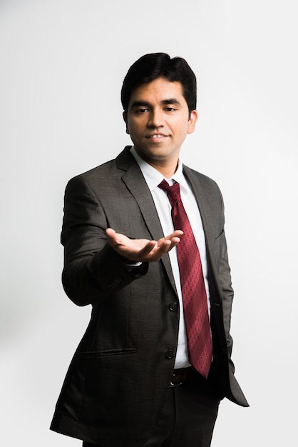 Indian Asian young businessman looking at a floating blue globe or earth model over right palm  while wearing complete corporate dress or attire like suit and tie, isolated over white background